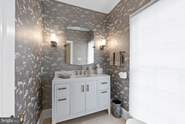 bathroom with wallpapered walls, vanity, and baseboards