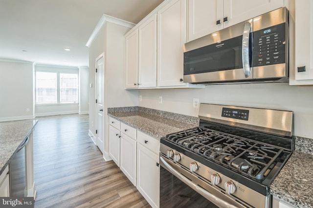 kitchen with light wood-style flooring, appliances with stainless steel finishes, white cabinets, and stone counters