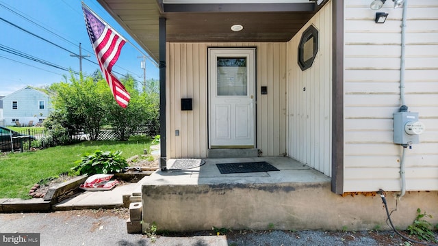 view of exterior entry with a lawn and fence