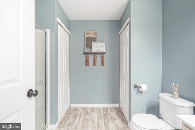 bathroom with a shower with shower door, wood finished floors, and toilet