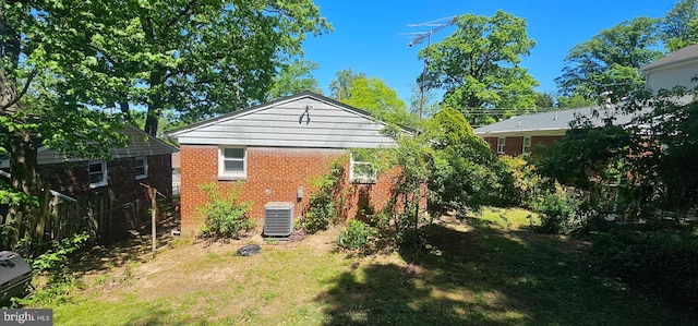 rear view of house with central AC unit, a yard, and brick siding