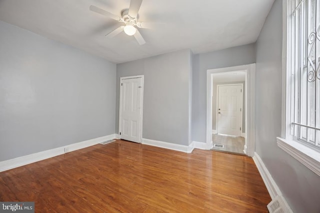 unfurnished room with baseboards, a ceiling fan, wood finished floors, and visible vents