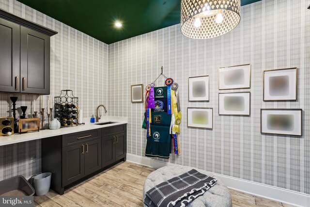 bathroom featuring a sink, baseboards, wood finished floors, and wallpapered walls