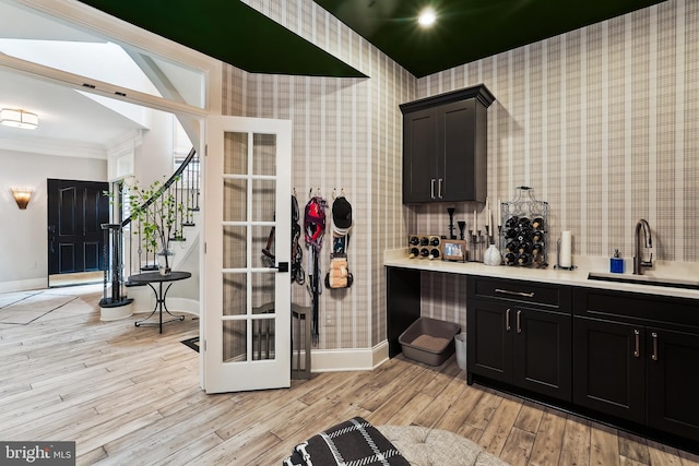 bathroom featuring a sink, baseboards, wallpapered walls, crown molding, and wood finished floors