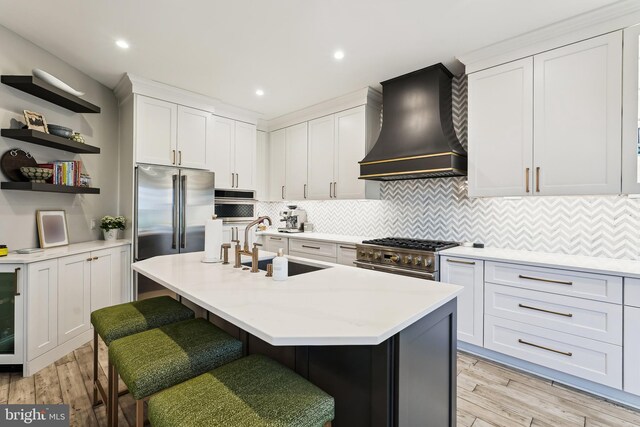 kitchen featuring custom exhaust hood, high end appliances, a sink, light wood-style floors, and recessed lighting
