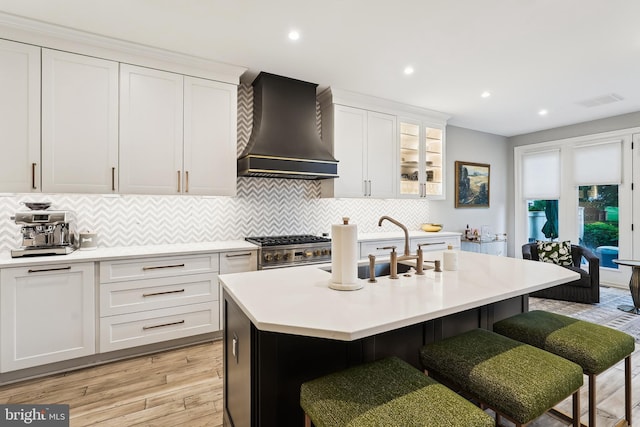 kitchen with custom exhaust hood, a sink, light wood-type flooring, a breakfast bar, and light countertops