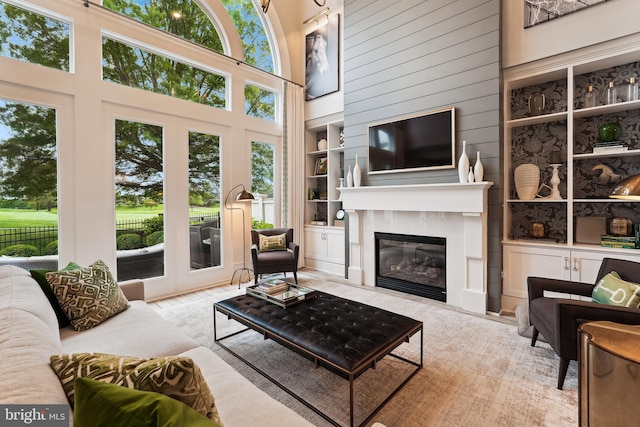 living area with built in features, healthy amount of natural light, french doors, a towering ceiling, and a glass covered fireplace