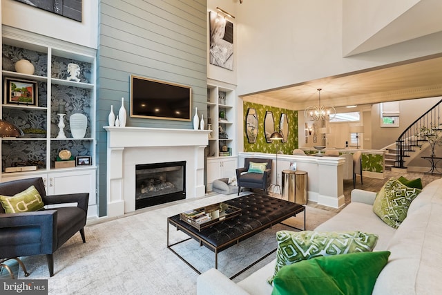 living area featuring a chandelier, built in features, a glass covered fireplace, stairway, and a towering ceiling