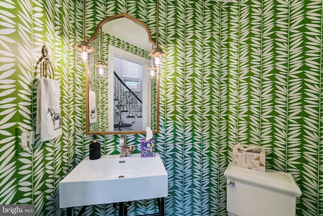 half bathroom with wallpapered walls, toilet, and a sink