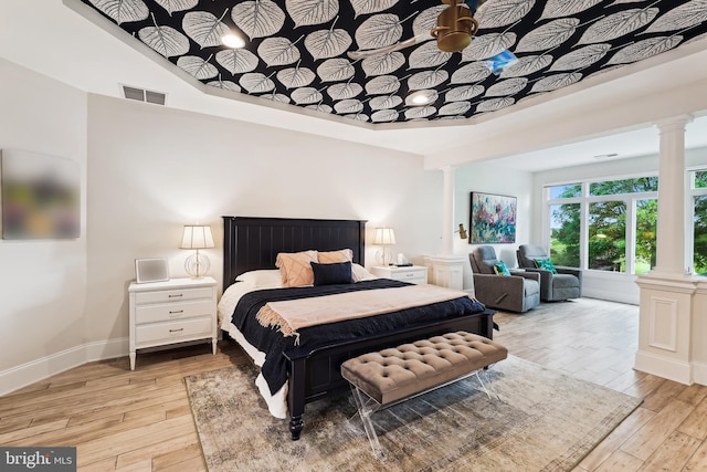 bedroom featuring decorative columns, light wood-style floors, and baseboards