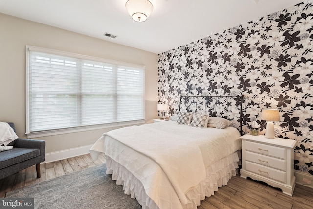 bedroom with baseboards, wood finished floors, multiple windows, and wallpapered walls