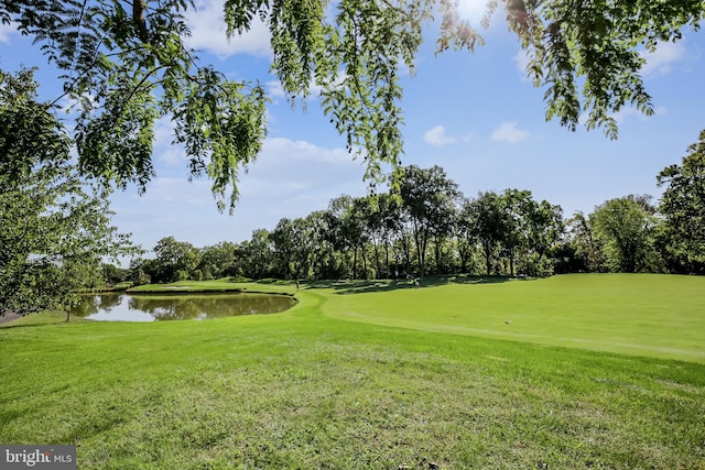 surrounding community with a water view, golf course view, a yard, and view of wooded area