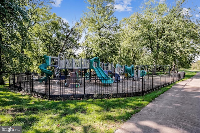 community play area featuring fence and view of wooded area
