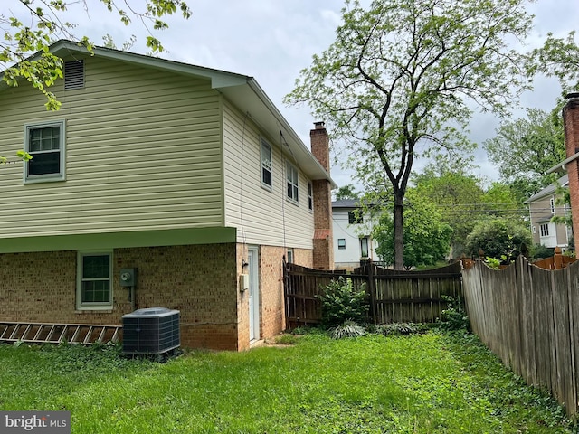 view of home's exterior featuring cooling unit, brick siding, fence, and a yard