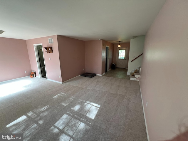 unfurnished living room featuring light colored carpet, visible vents, baseboards, and stairway