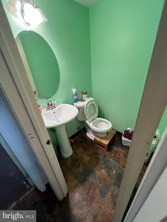half bathroom with a sink, toilet, and stone finish flooring