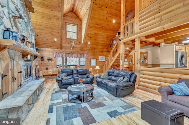 living room featuring high vaulted ceiling, stairway, light wood-style flooring, and a fireplace