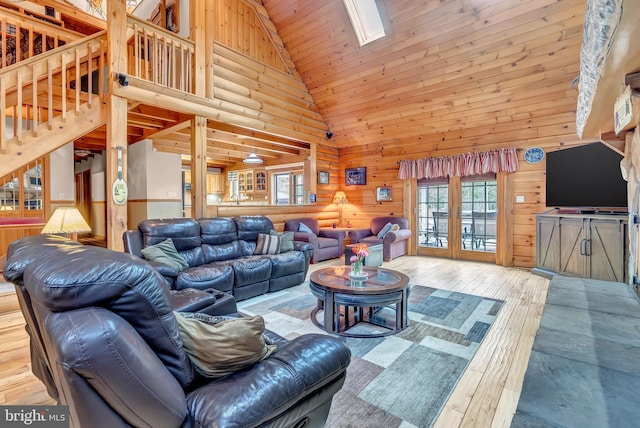 living room featuring hardwood / wood-style flooring, wood walls, a skylight, high vaulted ceiling, and stairs