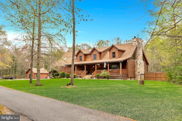 log cabin with a chimney, covered porch, fence, log exterior, and a front yard