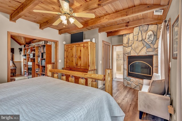 bedroom featuring connected bathroom, wood ceiling, a stone fireplace, light wood finished floors, and beam ceiling