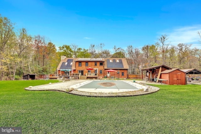 back of property with a patio, an outbuilding, a storage unit, a fenced in pool, and solar panels