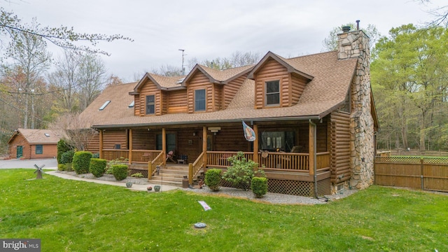 log-style house with fence, a porch, a shingled roof, and a front yard