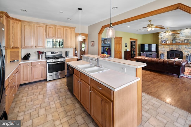 kitchen featuring light countertops, black appliances, ceiling fan, a stone fireplace, and a sink