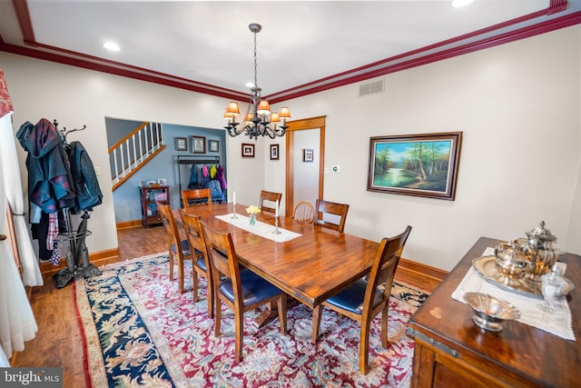 dining area with wood finished floors, stairs, ornamental molding, visible vents, and a notable chandelier