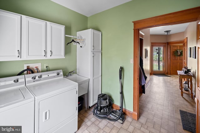 clothes washing area with cabinet space, washing machine and clothes dryer, a sink, baseboards, and brick patterned floor