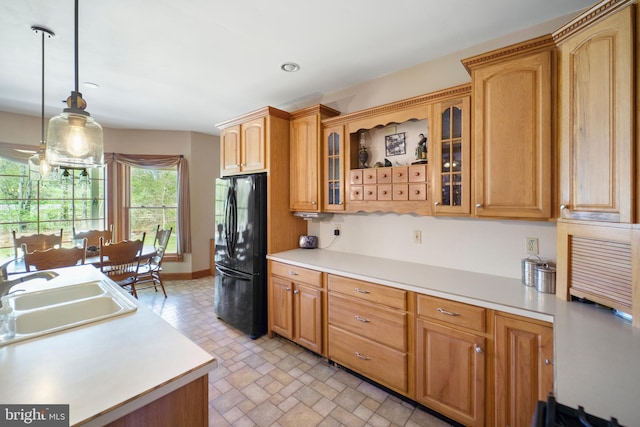 kitchen featuring glass insert cabinets, a sink, light countertops, freestanding refrigerator, and decorative light fixtures