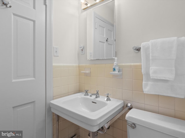 bathroom featuring tile walls, toilet, wainscoting, and a sink