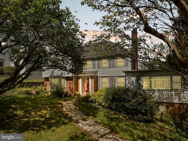 view of front of home with a chimney, brick siding, and a lawn