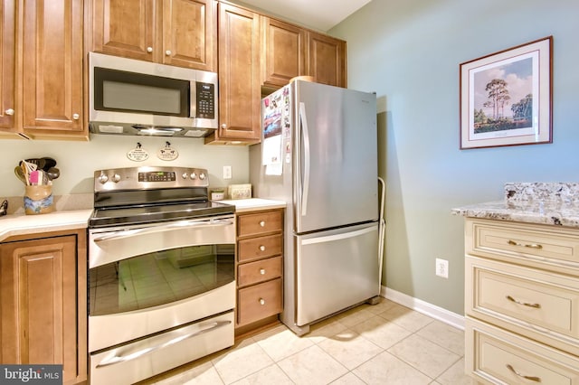 kitchen featuring brown cabinetry, light countertops, light tile patterned flooring, and stainless steel appliances