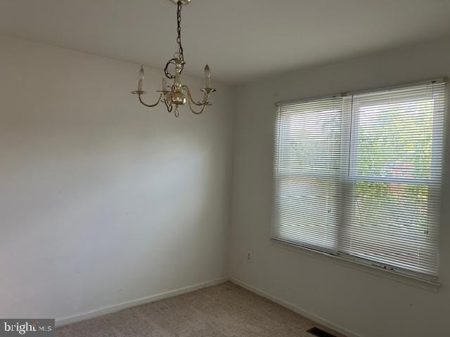 empty room featuring baseboards, a notable chandelier, and light carpet