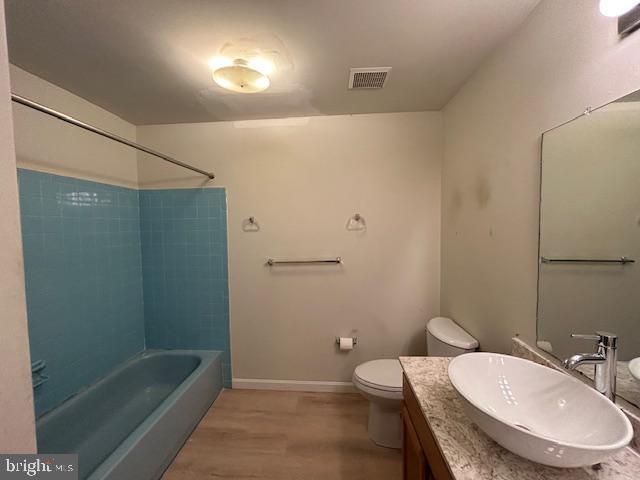 bathroom featuring vanity, toilet, tub / shower combination, wood finished floors, and visible vents