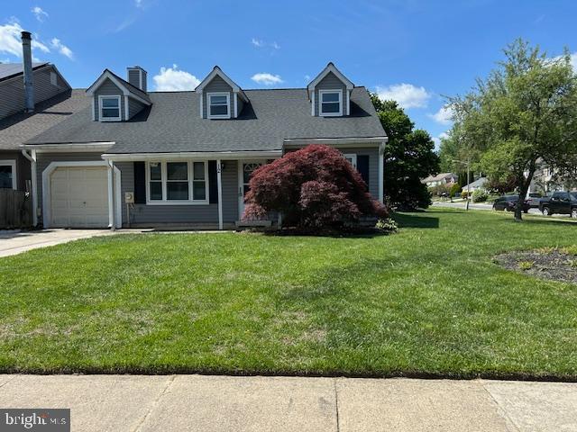 cape cod-style house with an attached garage, driveway, a chimney, and a front yard