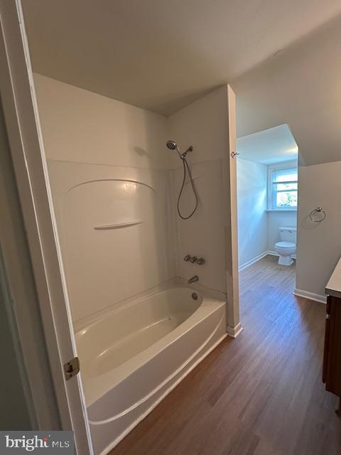 bathroom with wood finished floors, vanity, baseboards, toilet, and shower / bathtub combination