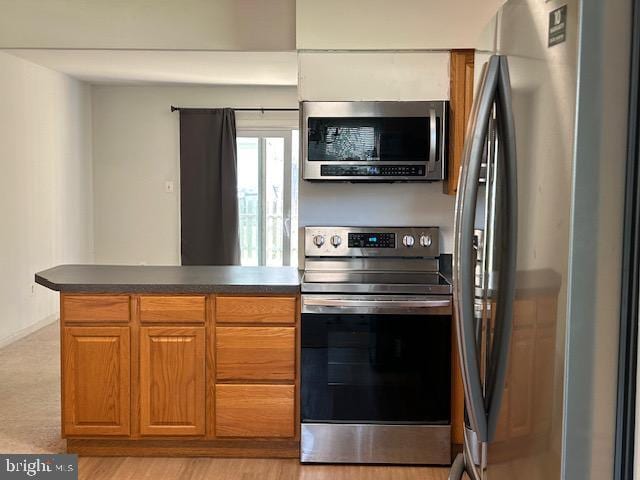 kitchen featuring brown cabinets, a peninsula, dark countertops, and appliances with stainless steel finishes