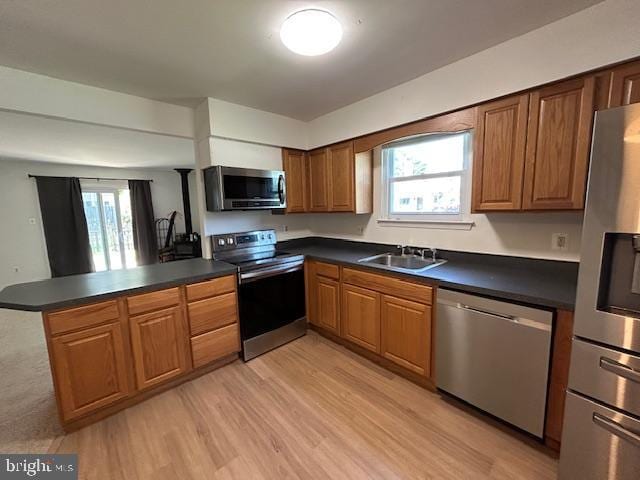 kitchen with dark countertops, appliances with stainless steel finishes, a sink, a peninsula, and light wood-style floors