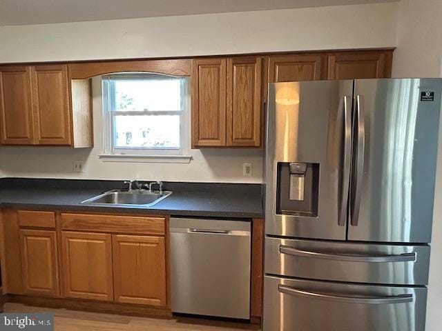 kitchen with brown cabinetry, a sink, dark countertops, and stainless steel appliances