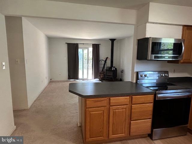 kitchen featuring stainless steel microwave, range with electric cooktop, dark countertops, and a wood stove