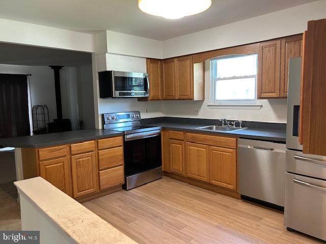 kitchen featuring appliances with stainless steel finishes, a sink, light wood finished floors, brown cabinetry, and a peninsula