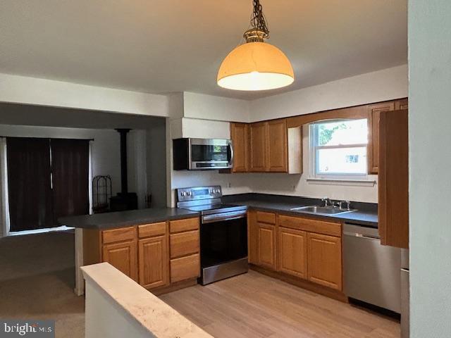 kitchen featuring a wood stove, a sink, a peninsula, stainless steel appliances, and light wood-style flooring