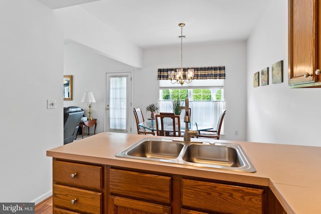 kitchen featuring an inviting chandelier, light countertops, brown cabinets, a sink, and decorative light fixtures