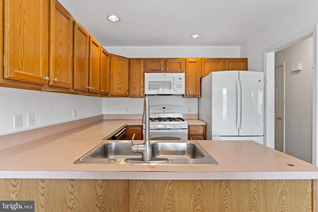 kitchen with brown cabinetry, light countertops, a sink, a peninsula, and white appliances