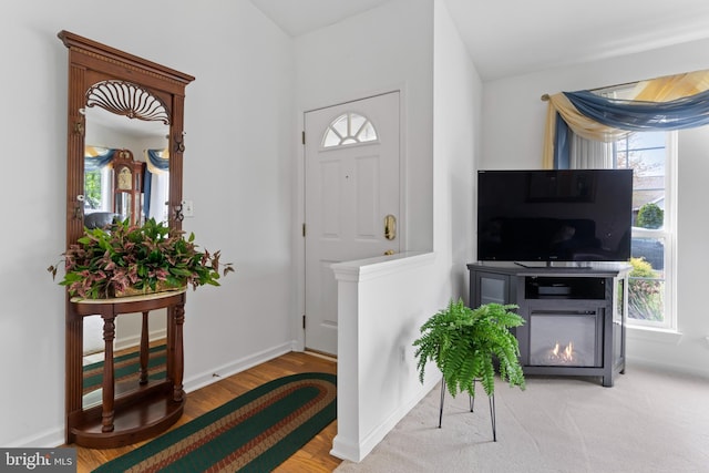 entrance foyer with baseboards, a lit fireplace, and wood finished floors