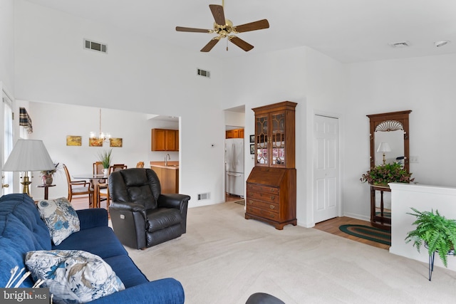 living area with light colored carpet, visible vents, and ceiling fan with notable chandelier