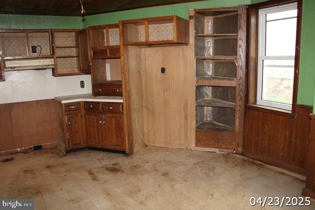 9635 Upper Strasburg Rd, Upperstrasburg, PA 17265 - kitchen with brown cabinetry, wainscoting, wooden walls, and under cabinet range hood