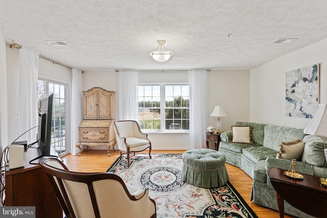 living area with a textured ceiling, visible vents, plenty of natural light, and light wood-style flooring