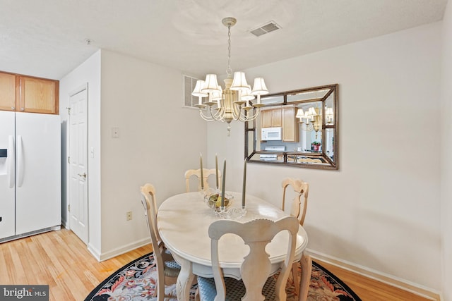 dining room featuring light wood-style flooring, visible vents, a chandelier, and baseboards